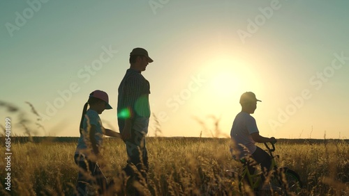 Father teaches boy, girl to ride children bike on road in countryside, sun. Child play, weekend with dad. Dad teaches children, son, daughter to ride bike, park, sunset. Family weekend. Happy family