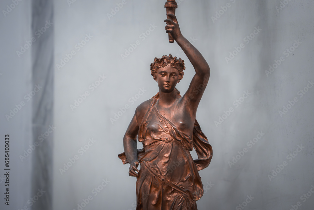 Bronze statue of woman holding torch on pedestal. Statue location and