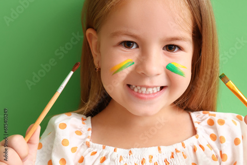 Cute little girl with paint brushes on green background, closeup