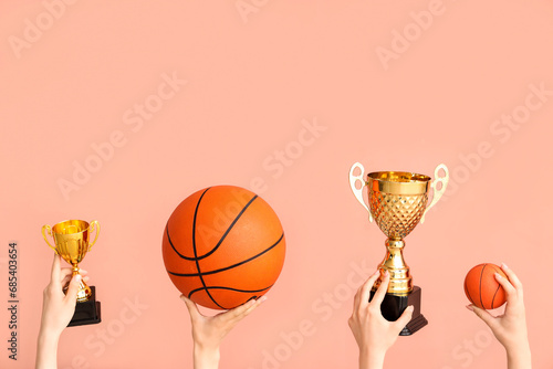 Female hands with gold cups and basketballs on pink background