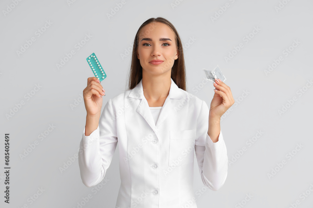 Female gynecologist with contraceptive pills and condoms on light background Female gynecologist with contraceptive pills and condoms on light background