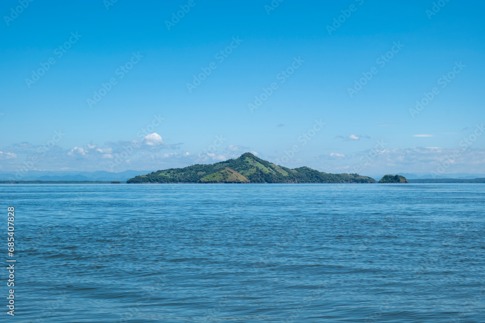 Island Seen From Afar with Volcanic Hills with Patches of Deforestation for Grazing and Forest in Front of a Calm Ocean