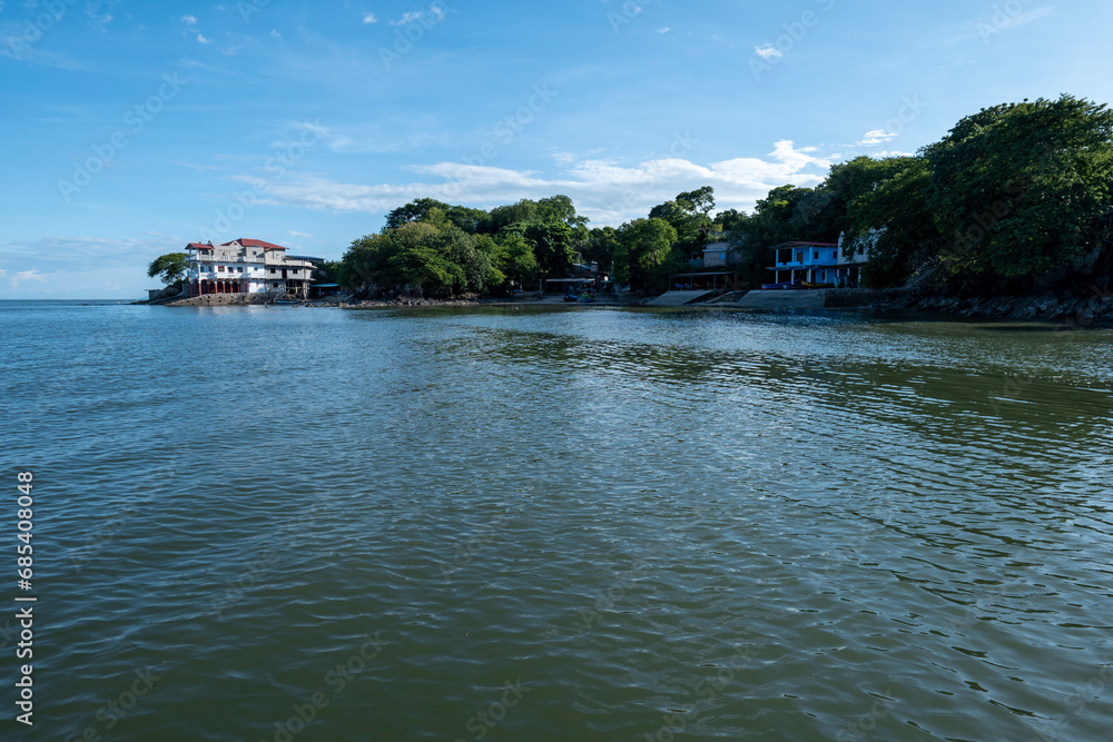 Paradisiacal Coastline Seen From Afar with Lush Vegetation Forest, and Colorful Houses by a Calm Ocean