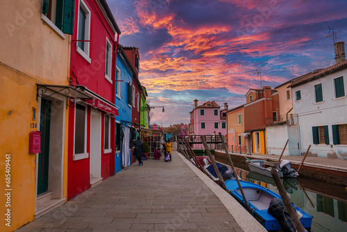 Colorful houses line a canal in Burano, Italy. The specific location and angle are unknown. No boats or gondolas are visible. Predominant colors, materials, and atmosphere are unspecified. © Aerial Film Studio