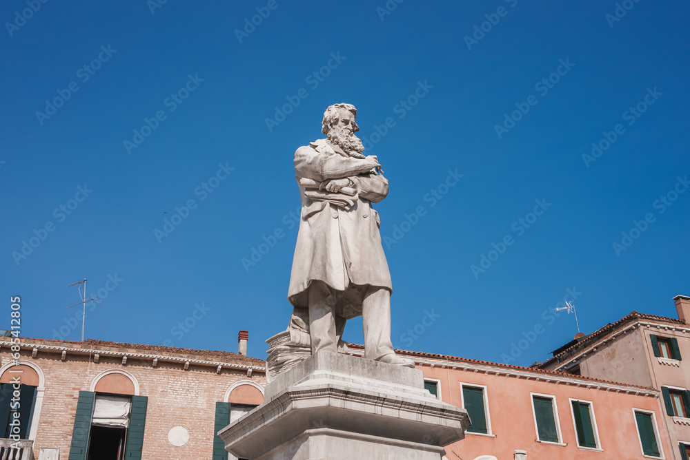Obraz premium A striking statue of a man in a long coat and hat stands in front of a building in Venice, Italy, adding to the city's rich history and charm.