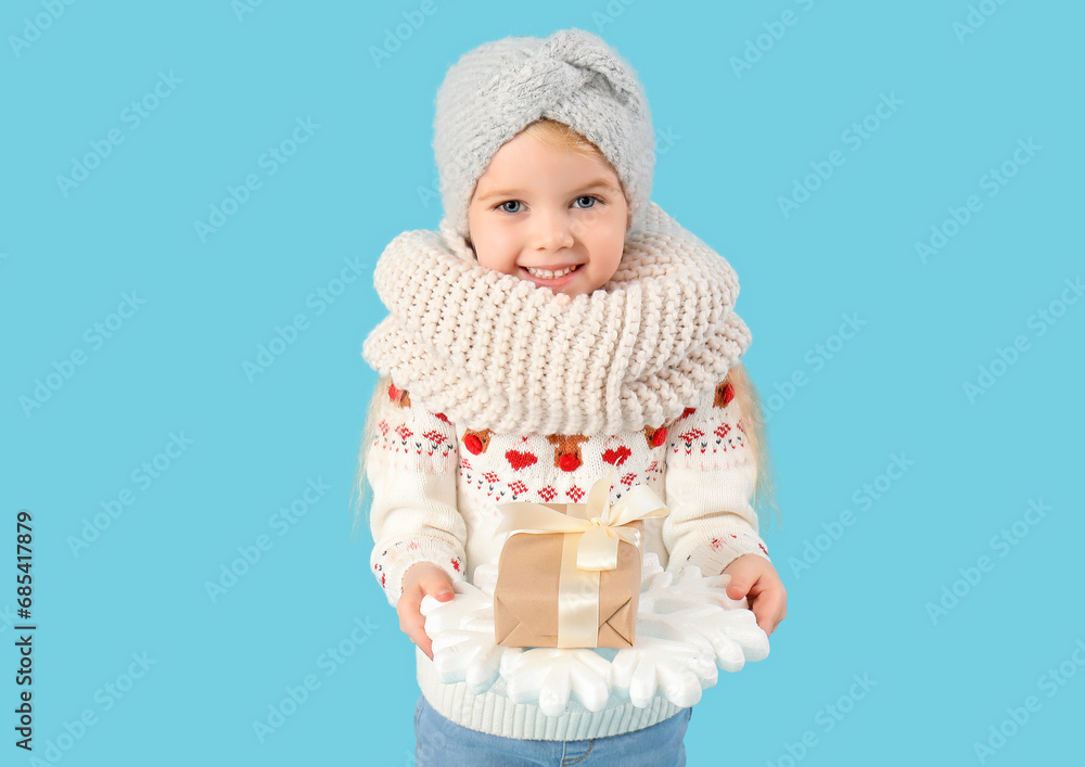 Cute little girl in winter clothes with gift box on blue background