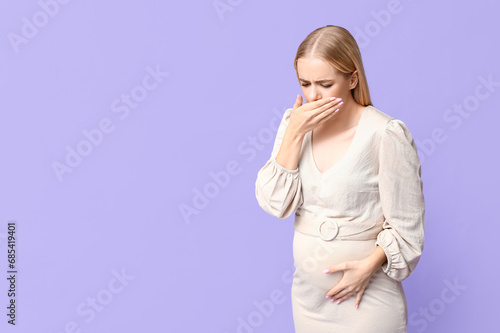 Beautiful young pregnant woman suffering from toxicosis on lilac background