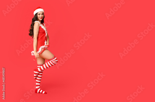 Beautiful young sexy woman in lingerie and Santa hat with whip on red background