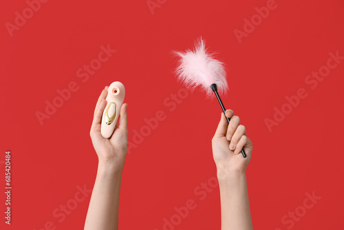 Female hands with vibrator and feather stick on red background, closeup