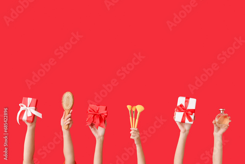 Female hands with different cosmetic items and gifts on red background