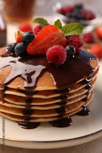 Stack of tasty pancakes with fresh berries, chocolate sauce and mint on white plate, closeup