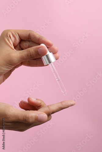 Woman applying cosmetic serum onto her finger on pink background, closeup