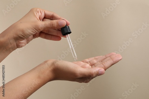 Woman applying cosmetic serum onto her hand on beige background  closeup. Space for text