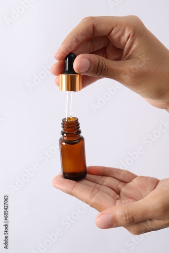 Woman with bottle of cosmetic serum and dropper on white background, closeup
