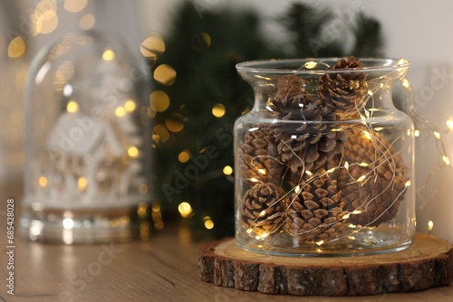Christmas decoration. Cones and festive lights in jar on wooden table  closeup. Space for text