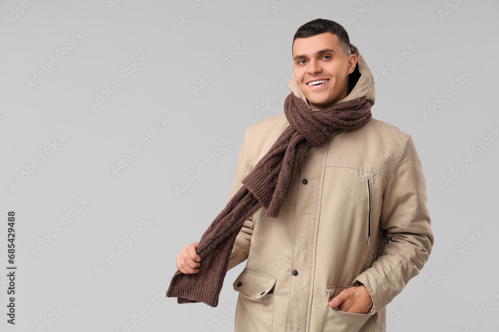 Young man in stylish puffer jacket and scarf on grey background Young man in stylish puffer jacket and scarf on grey background