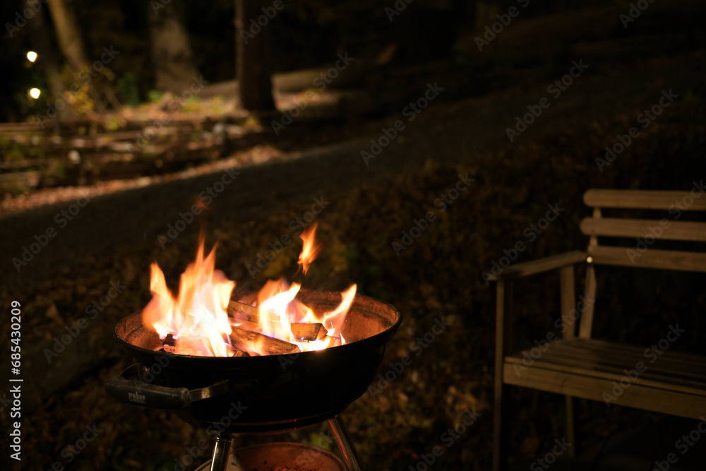 A glowing camp fire providing comfortable lights and barbecue grill pit with glowing and flaming of fire with hot charcoal briquettes with night time outdoor background A glowing camp fire providing comfortable lights and barbecue grill pit with glowing and flaming of fire with hot charcoal briquettes with night time outdoor background