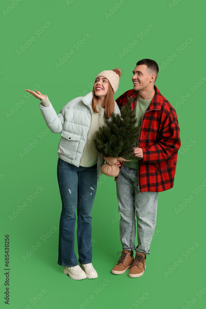 Beautiful young couple holding Christmas tree and pointing at something on green background Beautiful young couple holding Christmas tree and pointing at something on green background