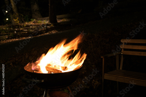A glowing camp fire providing comfortable lights and barbecue grill pit with glowing and flaming of fire with hot charcoal briquettes with night time outdoor background