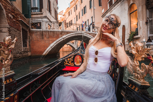 A serene gondola ride in Venice, Italy. A woman enjoys the picturesque scenery of traditional Venetian architecture and charming buildings lining the canal on a warm, sunny day.