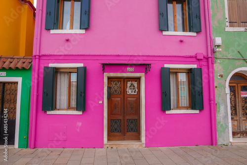 Vibrant pink house in Burano, Italy, with no landmarks or signage. Surrounding houses and material are unknown. No water, bridges, or vegetation visible. © Aerial Film Studio