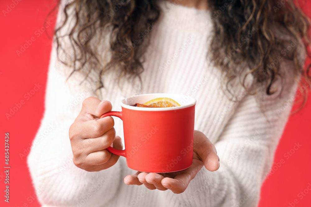 Young African-American woman with cup of hot mulled wine on red background Young African-American woman with cup of hot mulled wine on red background