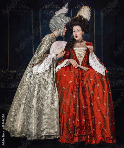 Two 18th century women standing close together gossiping 