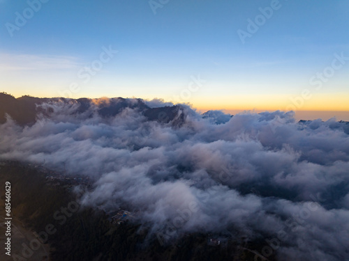 Aerial view of flowing fog waves on mountain tropical rainforest,Bird eye view image over the clouds Amazing nature background with clouds and mountain peaks in indonesia