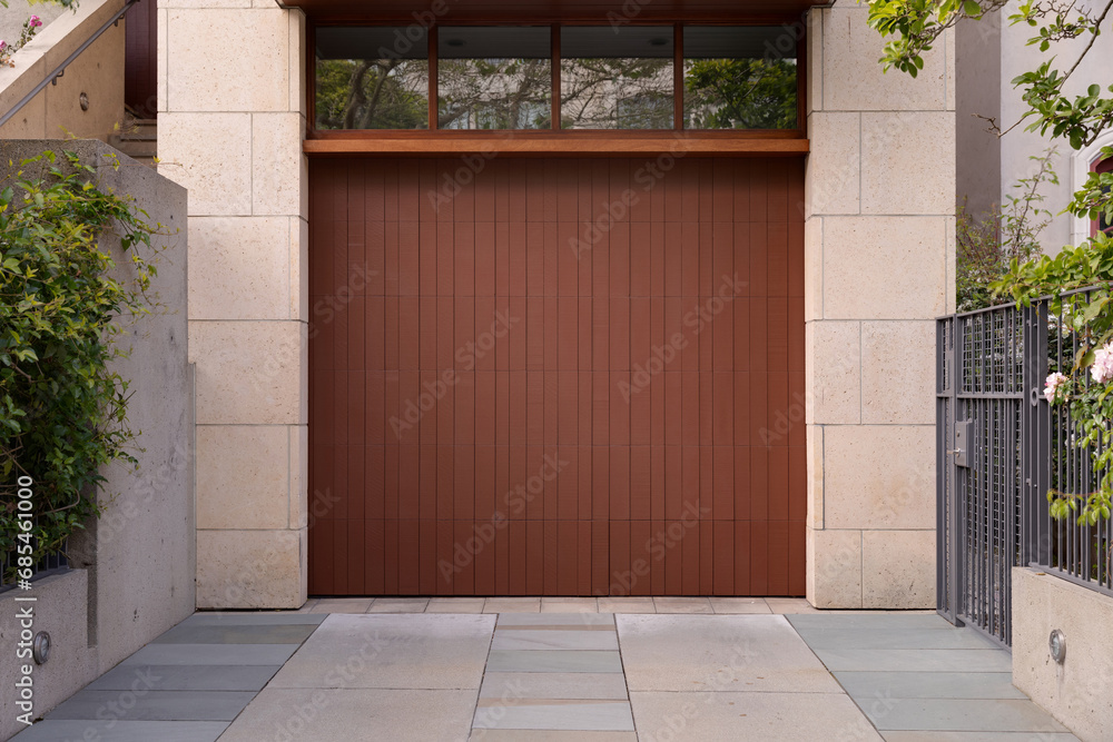 Brown garage door, off-white stone facade with small windows showing the reflection Brown garage door, off-white stone facade with small windows showing the reflection