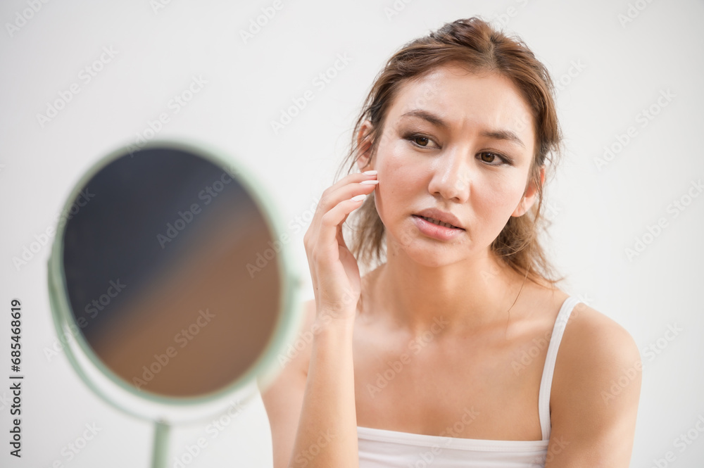 Young beautiful Asian woman checking her facial skin in mirror feeling worried about freckles wrinkles acne scar on face. Lady beauty self care skincare problem solution product advertising concept. Young beautiful Asian woman checking her facial skin in mirror feeling worried about freckles wrinkles acne scar on face. Lady beauty self care skincare problem solution product advertising concept.
