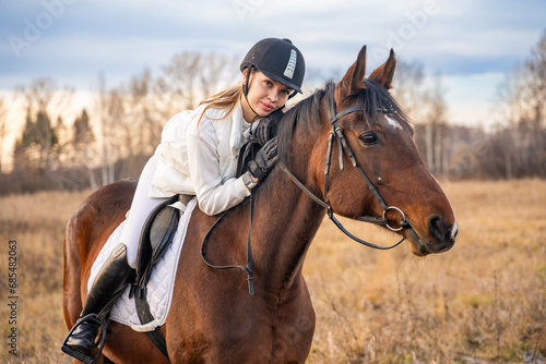 Beautiful blond professional female jockey lying on horse. Friendship with horse