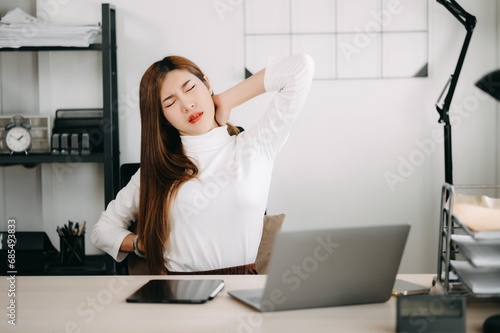 Overworked young Asian businesswoman office worker suffering from neck pain after had a long day. office syndrome concept. photo