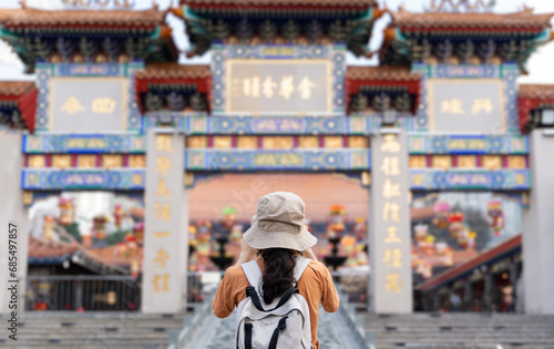Back view of tourist women blogger or Influencer are Taking photo while traveling in Hong Kong with the blur background of a most popular Chinese temple in travel and solo travel concept.