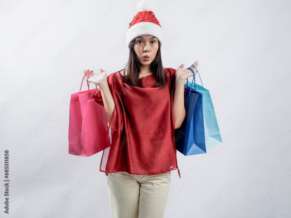 A portrait of a happy Asian woman celebrating Christmas, wearing a red dress and Santa hat, carrying a shopping bag. Isolated against a white background. A portrait of a happy Asian woman celebrating Christmas, wearing a red dress and Santa hat, carrying a shopping bag. Isolated against a white background.