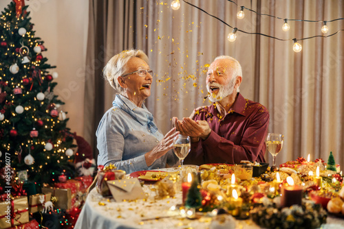 A festive christmas senior couple is celebrating christmas and new year's eve with confetti at home while sitting at christmas table.