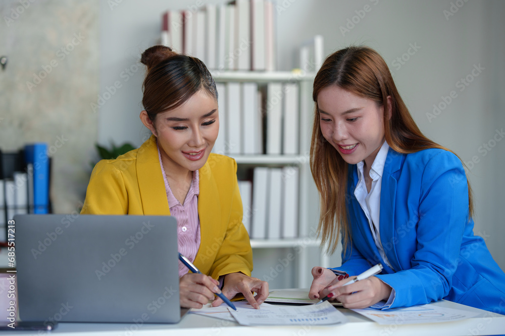 Two Asian businesswomen come up with an idea. Discuss investment projects and strategic planning with information via various documents and files. On a laptop computer at modern office. Two Asian businesswomen come up with an idea. Discuss investment projects and strategic planning with information via various documents and files. On a laptop computer at modern office.