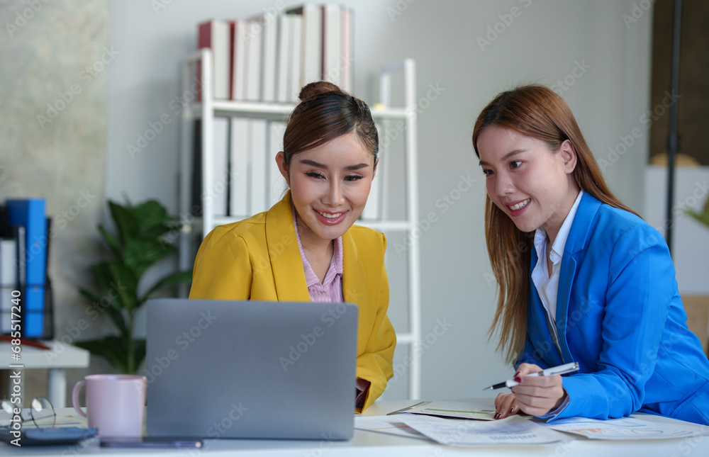 Two Asian businesswomen come up with an idea. Discuss investment projects and strategic planning with information via various documents and files. On a laptop computer at modern office. Two Asian businesswomen come up with an idea. Discuss investment projects and strategic planning with information via various documents and files. On a laptop computer at modern office.