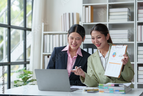Two confident Asian businesswomen discuss and present ideas via laptop online on new project to analyze joint planning, financial statistics and investment market at office.