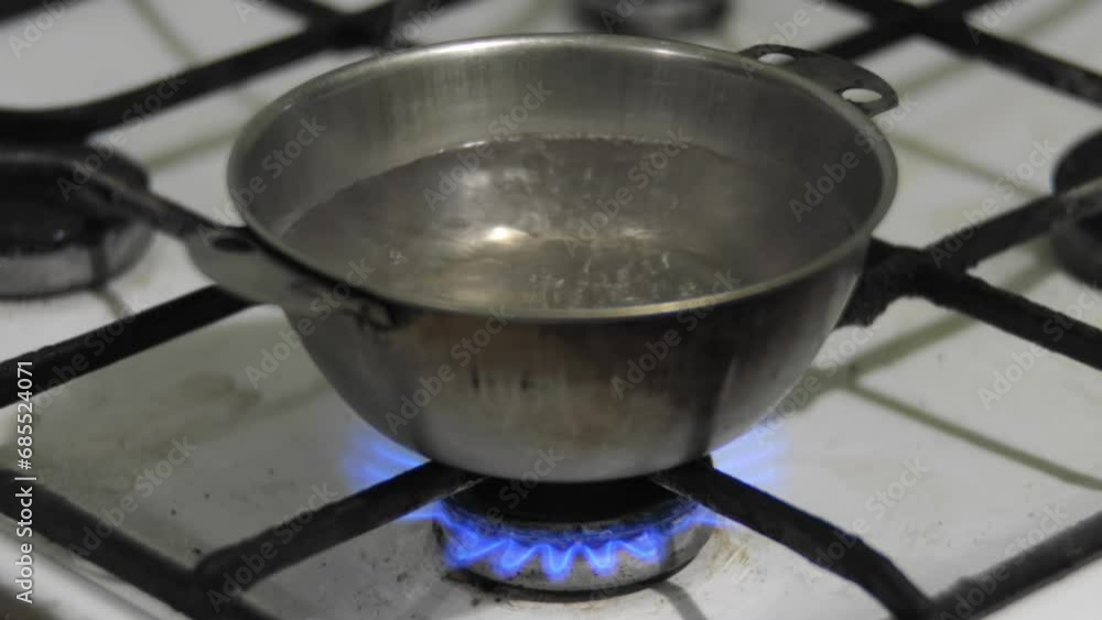 Water is boiling in a metal pot. Bowl of water warmed on a dirty old gas stove at home, close up. Poverty destitution misery concept Water is boiling in a metal pot. Bowl of water warmed on a dirty old gas stove at home, close up. Poverty destitution misery concept
