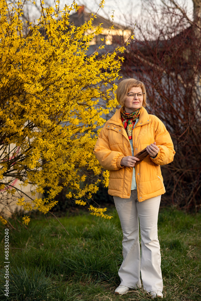 A beautiful woman waiting for a companion in spring against the background of blooming forsythia.