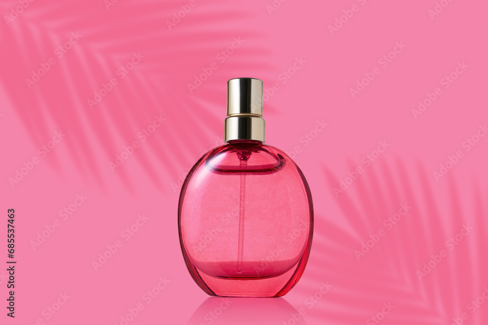 Transparent bottle of perfume on a pink background. Fragrance with palm leaves shadow. Transparent bottle of perfume on a pink background. Fragrance with palm leaves shadow.