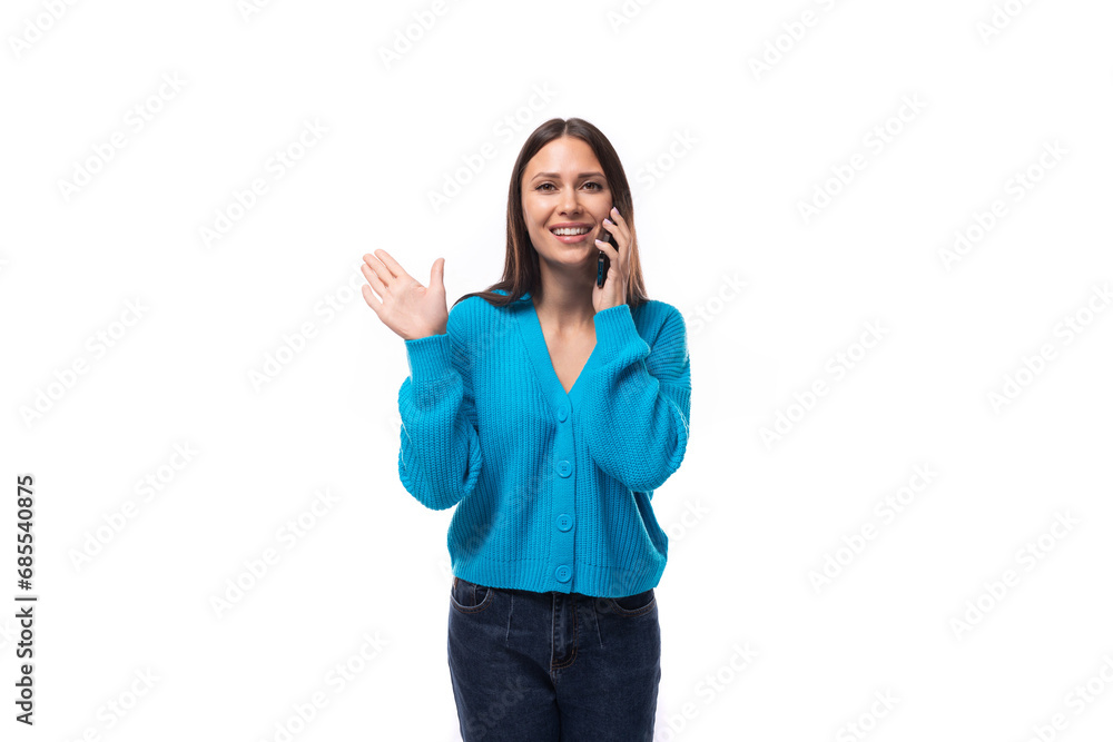 young pretty brunette lady dressed in a blue V-neck sweater speaks in a smartphone on a white background with copy space young pretty brunette lady dressed in a blue V-neck sweater speaks in a smartphone on a white background with copy space