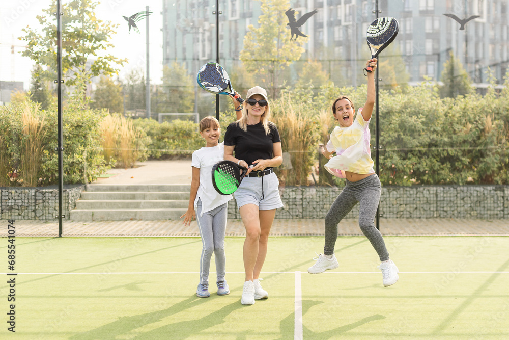 Obraz premium Young sporty woman with children playing padel game in court on sunny day
