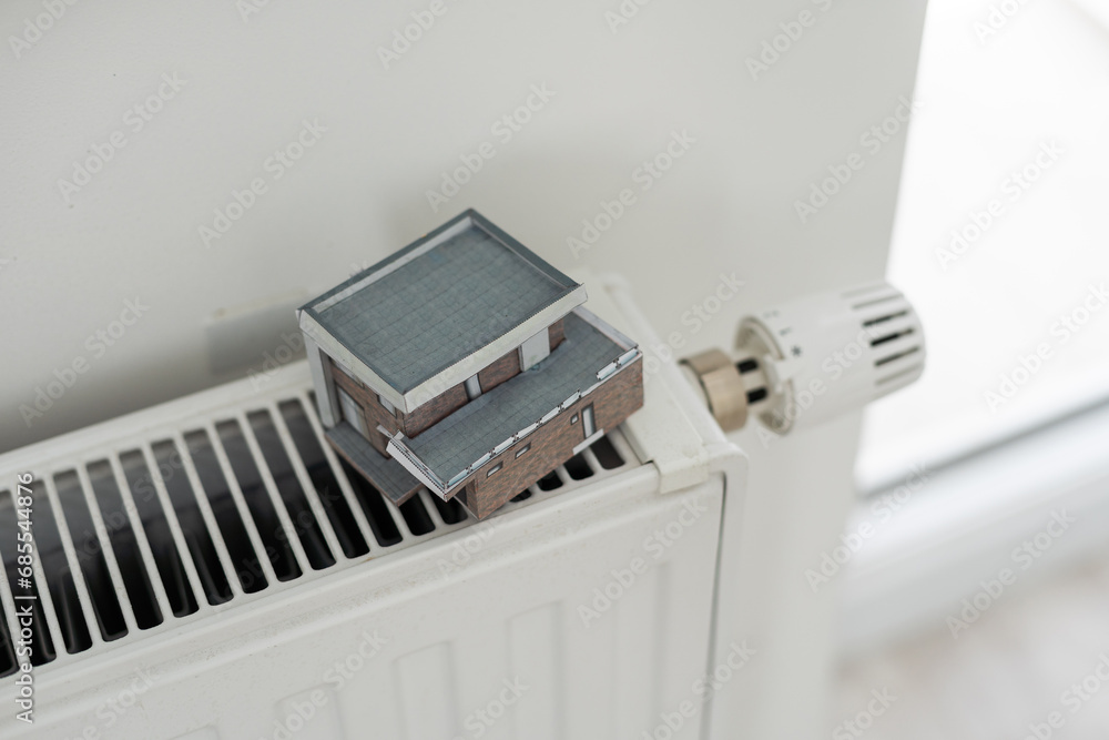 House model wrapped in scarf on radiator indoors, space for text. Winter heating efficiency House model wrapped in scarf on radiator indoors, space for text. Winter heating efficiency