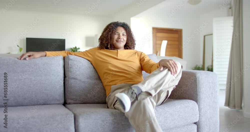 Portrait of happy biracial man with long hair sitting on sofa smiling in living room, slow motion Portrait of happy biracial man with long hair sitting on sofa smiling in living room, slow motion