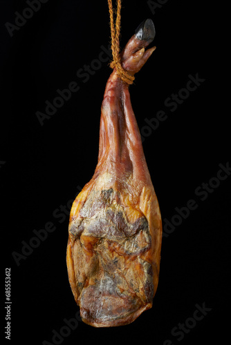 Delicious serrano ham hanging from a rope. Isolated on black. Gastronomy