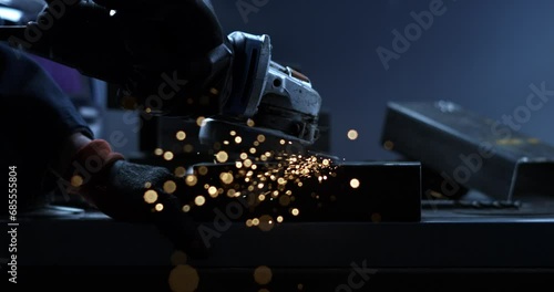 Super slow motion close up of blacksmith welder is smoothing metal steel with industrial angle grinder with flying sparks in workshop. photo