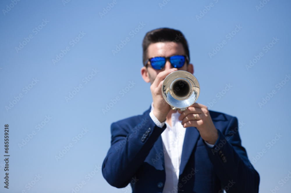 Handsome young businessman with a beard and a blue suit playing the trumpet. The man is a musician in his spare time and music is one of his great passions. Handsome young businessman with a beard and a blue suit playing the trumpet. The man is a musician in his spare time and music is one of his great passions.