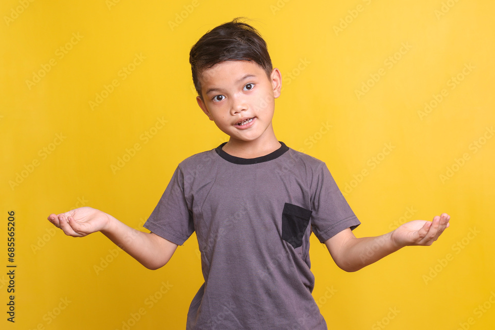 Young Asian boy wearing casual t-shirt showing both hands open palms, presenting comparison and balance isolated over yellow background Young Asian boy wearing casual t-shirt showing both hands open palms, presenting comparison and balance isolated over yellow background