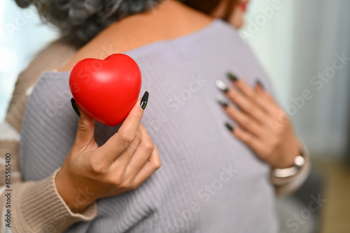 Young woman holding red heart while hugging senior mother . Health care, insurance and world heart day concept